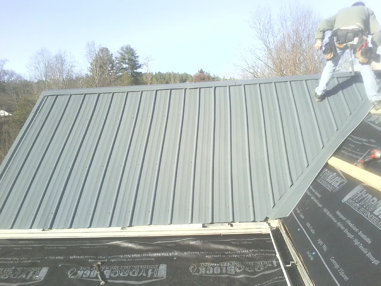 Crew installing dark green standing seam panels over synthetic underlayment in Medina