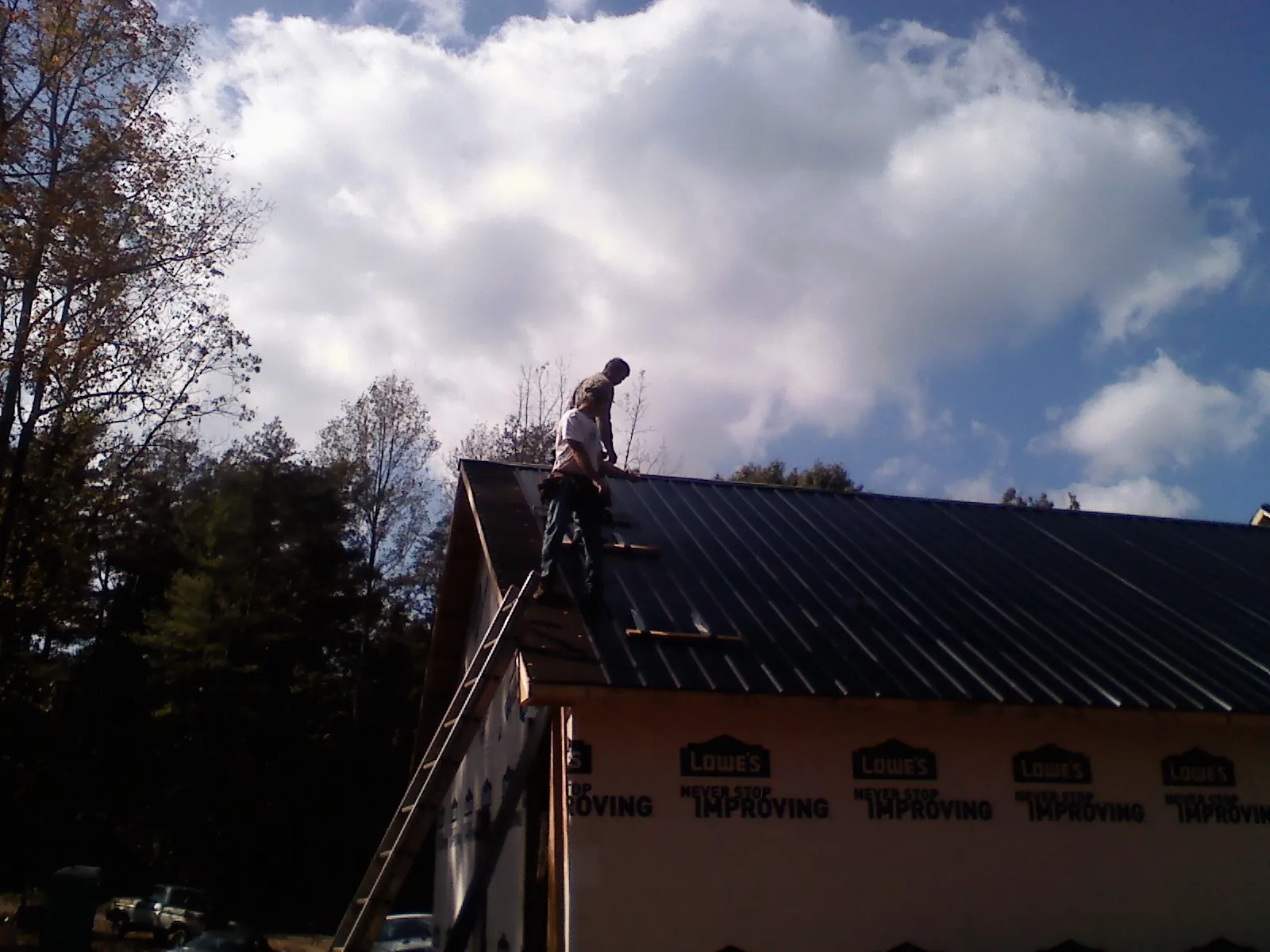 Roofer fastening dark metal panels high against a cloudy sky, from a Roof Inspection job in Medina